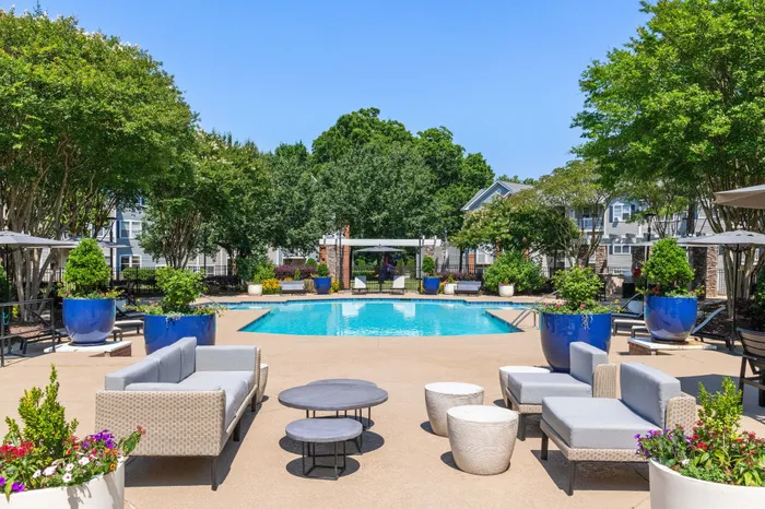 Luxurious apartment community featuring a stunning outdoor pool area with modern seating, lush greenery, and vibrant blue planters.