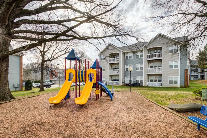 Inviting apartment complex with cheerful playground featuring vibrant slides, surrounded by lush greenery.