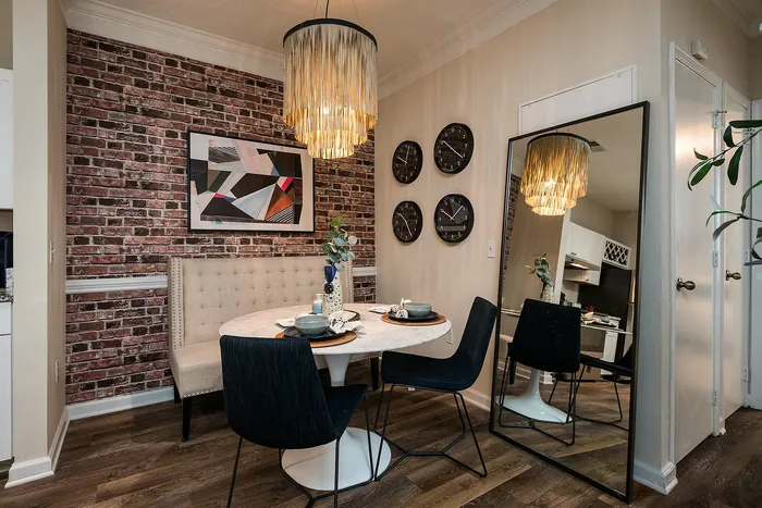 Chic dining area with modern decor featuring a round table, stylish chairs, and a vibrant abstract painting on a trendy brick wall.