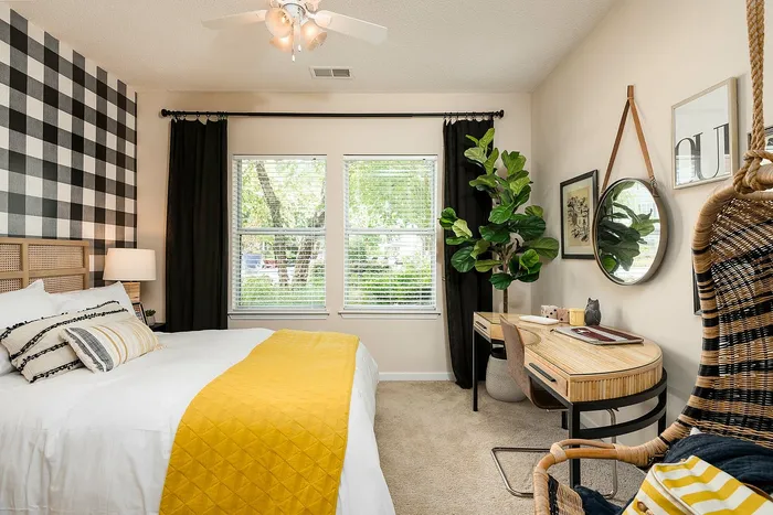 Chic bedroom with stylish plaid accent wall, vibrant yellow bedding, and a cozy workspace featuring natural light and a lush indoor plant.