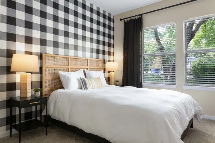 Elegant bedroom featuring a cozy wooden headboard, chic black and white checkered accent wall, and large windows with lush greenery views.