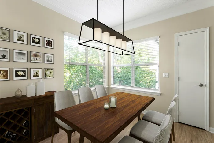Bright dining room with elegant wooden table and modern chandelier, surrounded by large windows with green views.