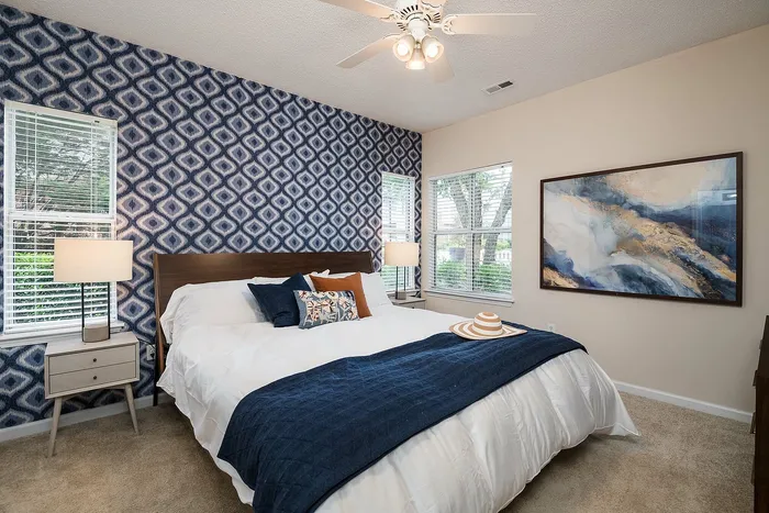 Elegant bedroom with a stylish patterned accent wall, cozy white bedding, and large windows providing abundant natural light.