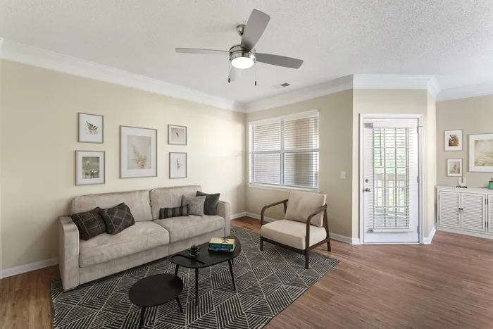Modern living room with cozy beige sofa, stylish armchair, elegant rug, and wall art, featuring abundant natural light from large windows.