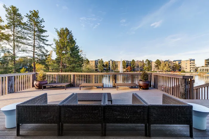 Breathtaking apartment balcony with elegant wicker furniture overlooking a tranquil pond and lush trees.