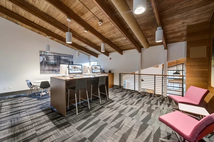 Modern loft-style office space with sleek wooden ceiling, contemporary seating, and multiple computer workstations.