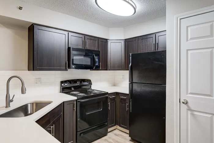 Modern kitchen with sleek dark cabinetry, black appliances, and elegant white countertops.