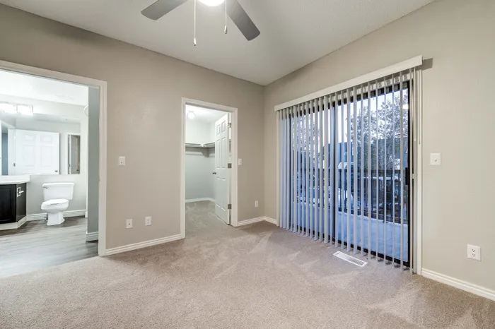 Bright bedroom with modern ceiling fan, showcasing a spacious walk-in closet, adjoined elegant bathroom, and floor-to-ceiling glass doors leading to a scenic balcony view.