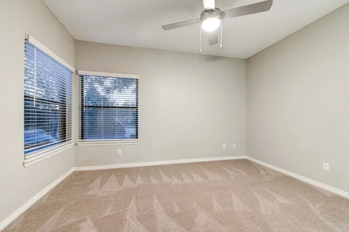 Spacious bedroom with plush carpeting and large windows showcasing serene views, complemented by a sleek ceiling fan for optimal comfort.