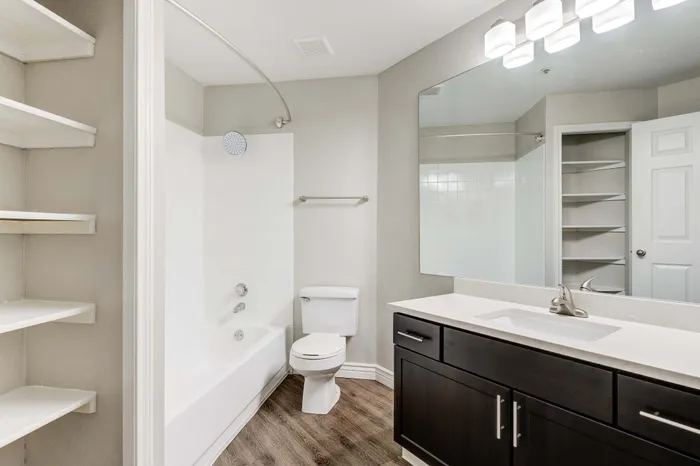 Modern bathroom featuring elegant dark wood cabinetry, a spacious mirror, and sleek fixtures complemented by clean white tiles.