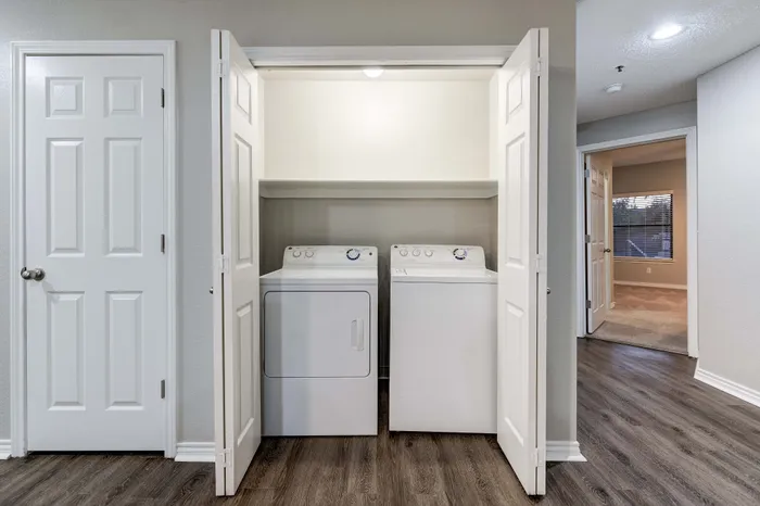 Modern apartment laundry nook with sleek washer and dryer, accented by elegant white bi-fold doors and stylish wood flooring.