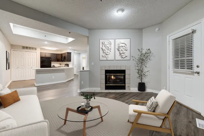 Modern open-concept living room with cozy fireplace, stylish artwork, and a spacious kitchen featuring dark cabinetry and sleek countertops.