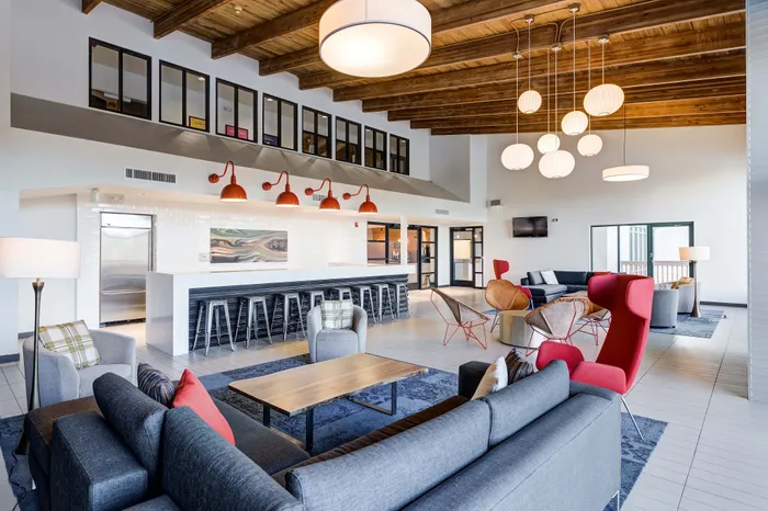 Modern communal lounge with stylish seating, vibrant red accents, and a sleek bar area under warm wooden ceilings.