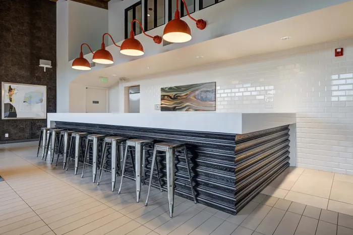 Chic and modern communal area with sleek metal barstools, vibrant red pendant lights, and a contemporary white brick backsplash.