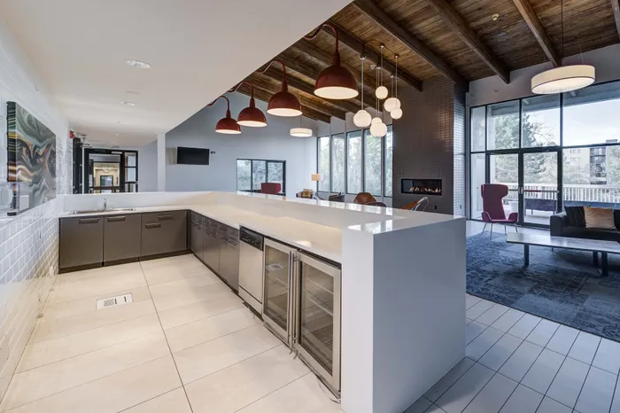 Modern open-plan kitchen and living area featuring sleek cabinetry, stylish pendant lighting, and a cozy fireplace with large windows offering scenic outdoor views.