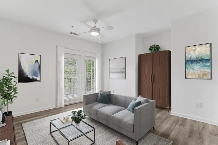 Modern living room with stylish gray sofa, elegant artwork, and a light-filled space featuring large windows and wood flooring.