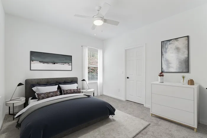 Elegant bedroom featuring a cozy gray bed, modern white furniture, and chic abstract artwork, complemented by a soft carpet and natural light through the windows.