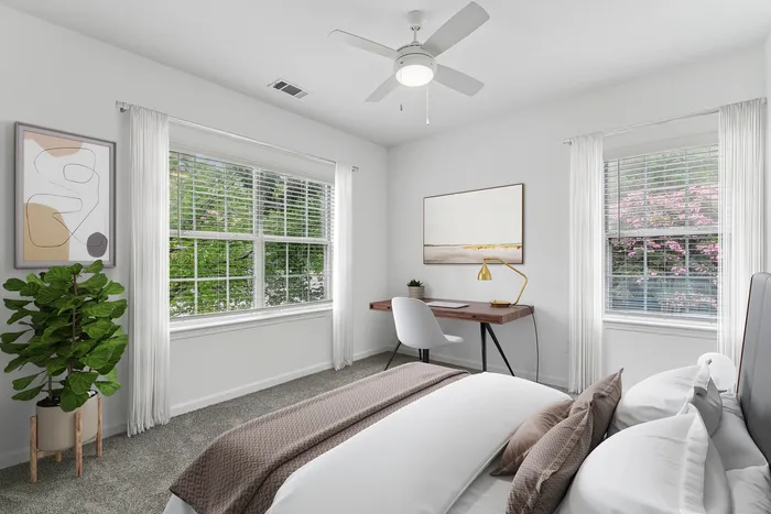 Bright and inviting bedroom with minimalist decor, featuring large windows, a cozy workspace, and lush greenery.