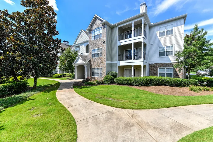 Charming apartment complex featuring elegant balconies, surrounded by lush greenery and a welcoming path.