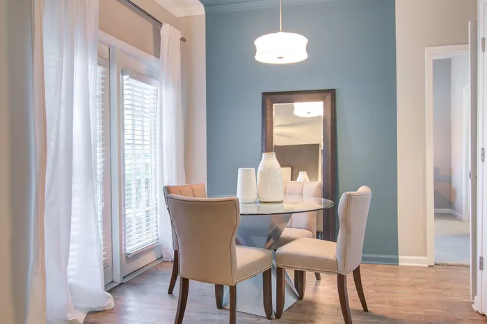 Elegant dining area with a round glass table, stylish chairs, and soft natural light through large windows for a cozy ambiance.