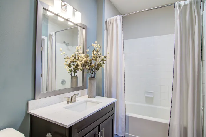 Elegant bathroom with a sleek vanity, bright lighting, and a modern bathtub, complemented by tasteful floral decor.