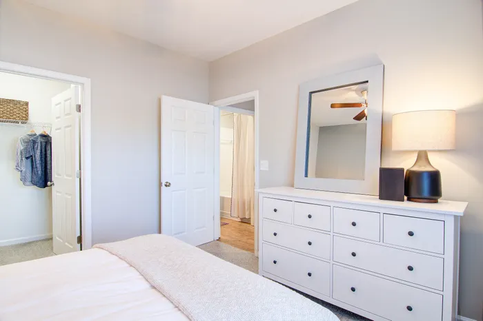 Bright and inviting bedroom featuring a modern dresser, elegant decor, and a glimpse of the walk-in closet and bathroom, perfect for stylish living.