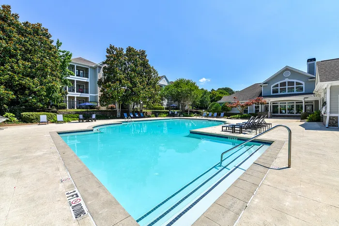 Gorgeous outdoor pool area with pristine blue water surrounded by lush greenery and modern apartment buildings, offering a tranquil retreat for residents.