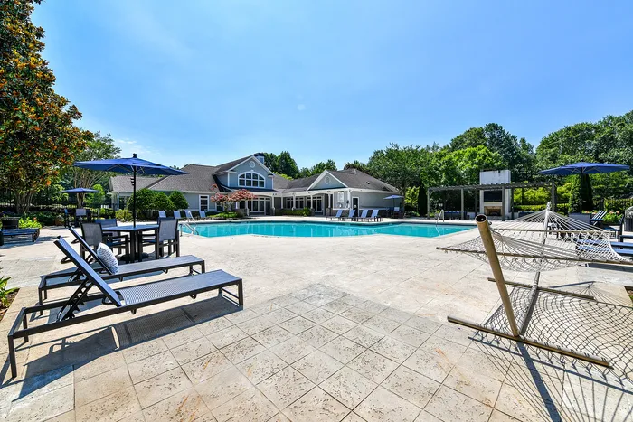 Luxurious outdoor pool area with stylish lounge chairs, shaded tables, and a relaxing hammock, set against a beautiful clubhouse backdrop.