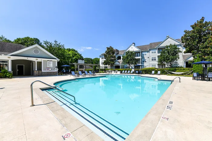 Inviting apartment complex with a sparkling swimming pool, sun loungers, and lush greenery, perfect for relaxation and enjoyment.