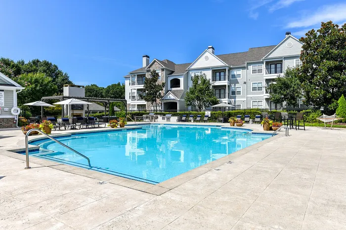 Luxurious apartment complex with a pristine swimming pool and sun loungers under bright blue skies, offering a serene environment for relaxation.