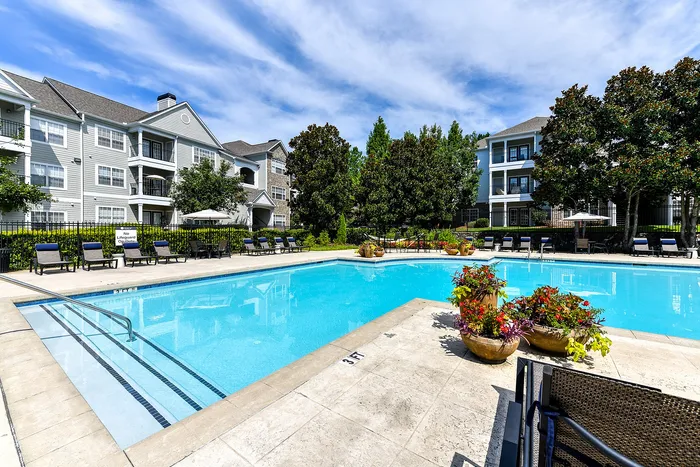 Inviting apartment complex with a sparkling pool, surrounded by lush greenery and comfortable lounge chairs.