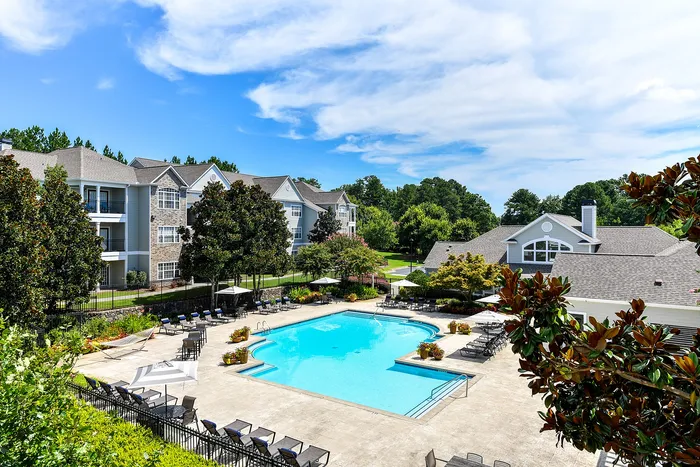 Charming apartment complex with a sparkling swimming pool surrounded by lush greenery, offering a tranquil and inviting living environment.
