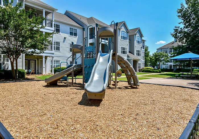 Charming apartment complex with a vibrant playground, nestled in a lush green setting, perfect for family living.