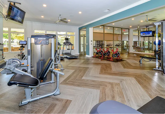 Modern fitness center with state-of-the-art equipment, including treadmills and stationary bikes, set in a spacious, bright room with stylish wood-patterned flooring.