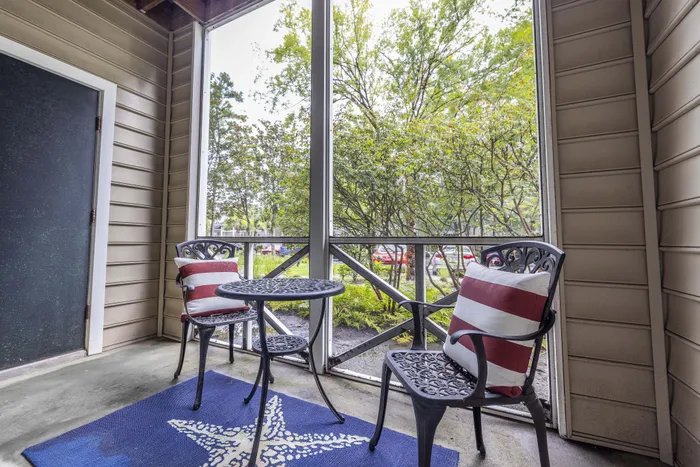 Cozy screened patio with two elegant chairs and a small table, surrounded by lush greenery, offering a peaceful retreat.