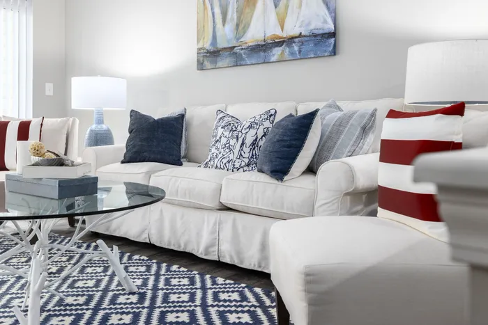 Chic living room with a cozy white sofa adorned with stylish pillows, modern glass coffee table, and elegant blue accents.