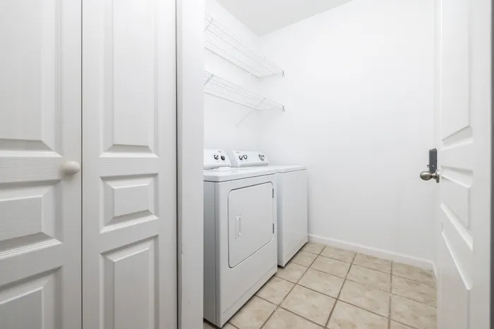 Modern laundry room featuring a sleek washer and dryer set with ample shelving, accentuated by stylish tile flooring.