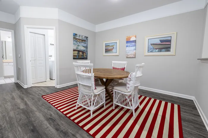 Elegant dining area with white wicker chairs, round wooden table, and vibrant red striped rug in a modern apartment.