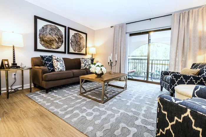 Elegant living room with modern decor, featuring a plush brown sofa, stylish armchairs, and a wooden coffee table. Large windows invite natural light, highlighting the cozy atmosphere and chic design.