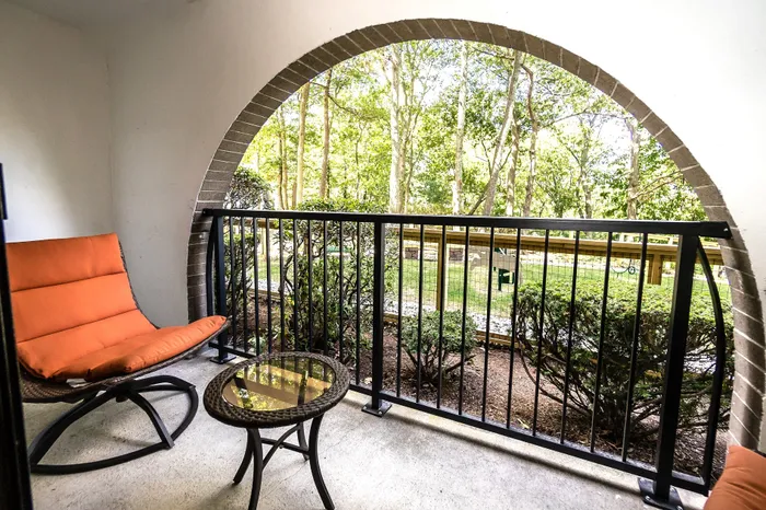 Charming outdoor balcony with cozy orange seating, arched brick detail, and lush green garden views.
