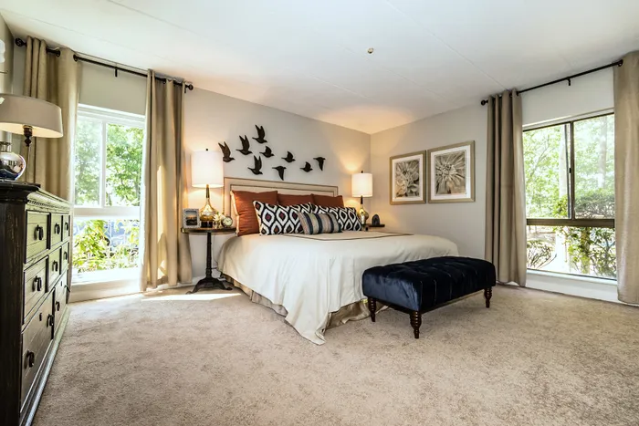 Elegant bedroom with plush carpeting, large windows, stylish wall art, and a cozy bed with vibrant pillows.