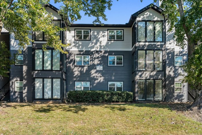 Modern apartment building with large windows, surrounded by lush greenery and bathed in natural sunlight.