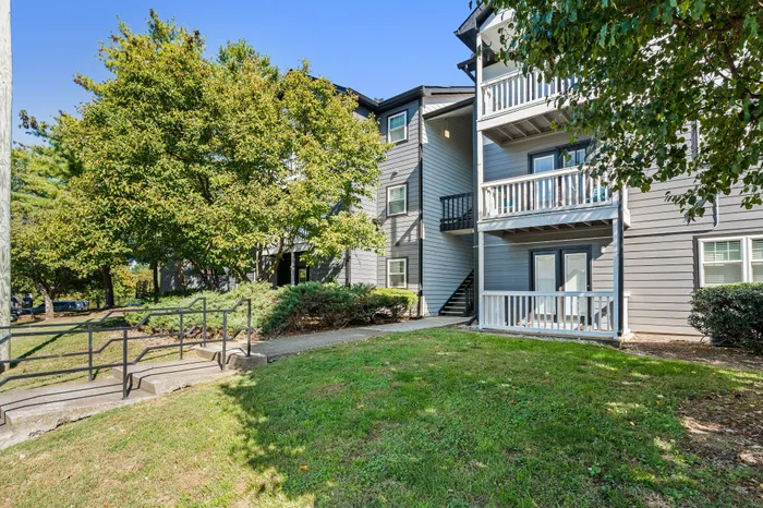 Charming apartment exterior with welcoming balconies surrounded by lush greenery and a well-maintained pathway.