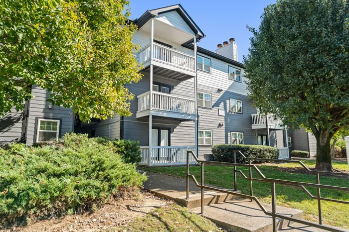Charming multi-level apartment building with private balconies, surrounded by lush greenery and mature trees, offering a serene residential setting.