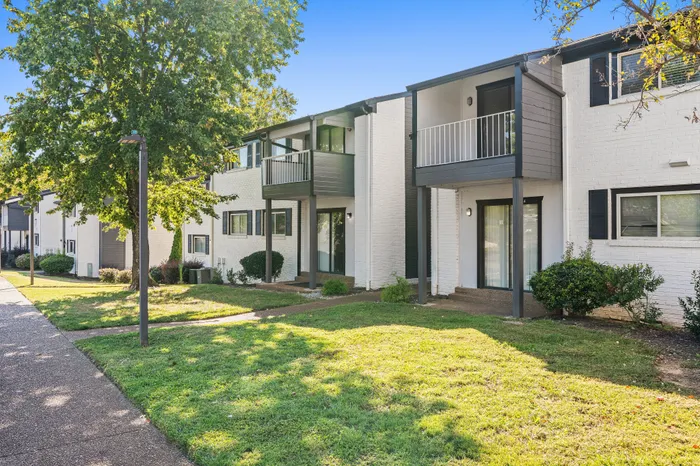Charming apartment building with inviting balconies, surrounded by lush greenery and a bright, sunny atmosphere.
