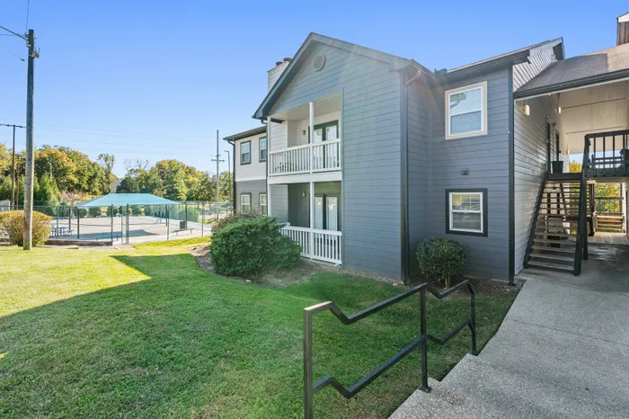 Charming apartment exterior with a private balcony, nestled in lush greenery, featuring clean architectural lines and adjacent to a recreational area.