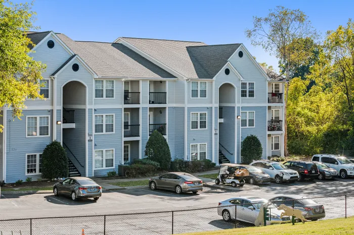 Charming modern apartment complex with spacious balconies, ample parking, and surrounded by lush greenery on a sunny day.