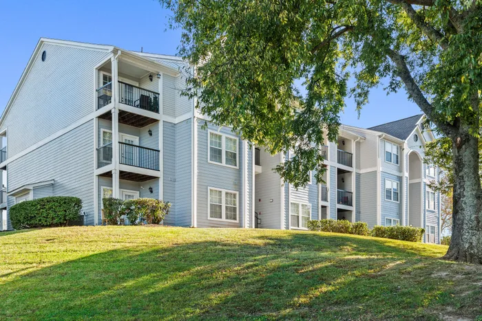 Charming apartment complex with spacious balconies, surrounded by lush greenery and bright blue skies.