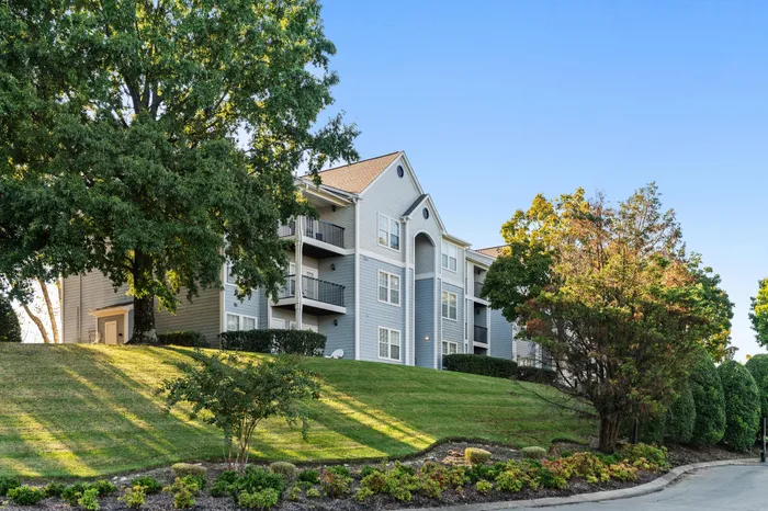 Charming apartment building with elegant balconies, nestled in a lush landscape with verdant trees and manicured lawn.