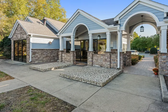 Charming modern entrance with decorative stonework, large windows, and inviting arches surrounded by lush greenery.